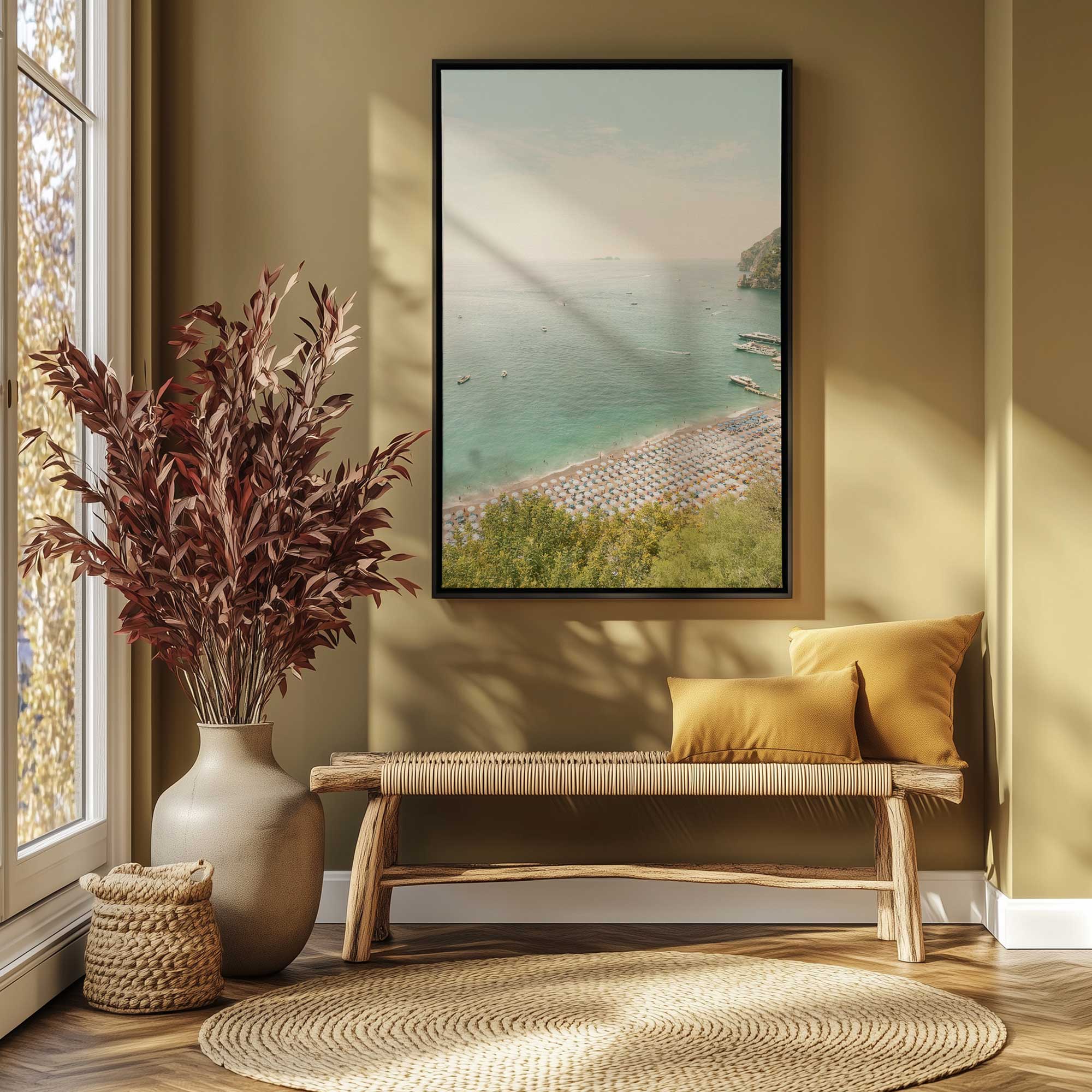 amalfi shoreline view on canvas in a black frame hanging above a bench with yellow cushions, a woven rug and dried branches